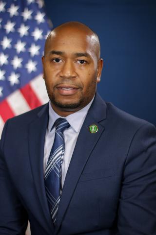 Man in suit and tie smiling, standing in front of an American flag.