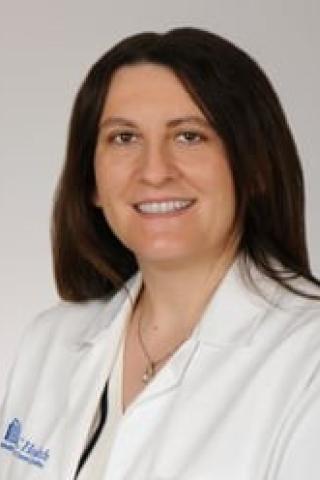 A smiling woman in a white lab coat with a blue logo.