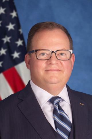Executive Medical Center Director Griffith in suit and tie sitting in front of an American flag.