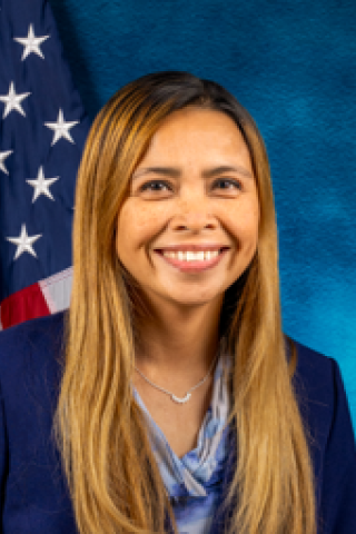Woman with long blonde hair smiling in front of American flag.