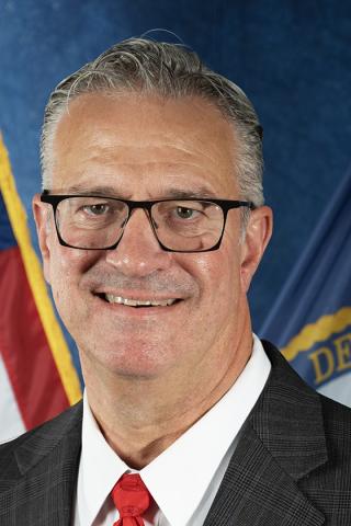 Man in suit and red tie smiling in front of American flag.