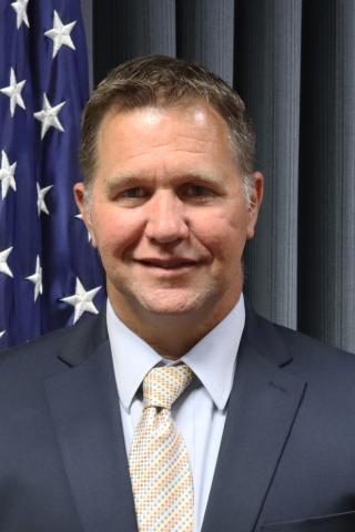 Man in business suit smiles in front of American flag.