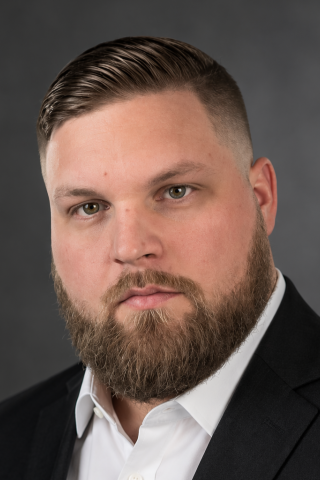 Man in black suit and white shirt with thick beard.