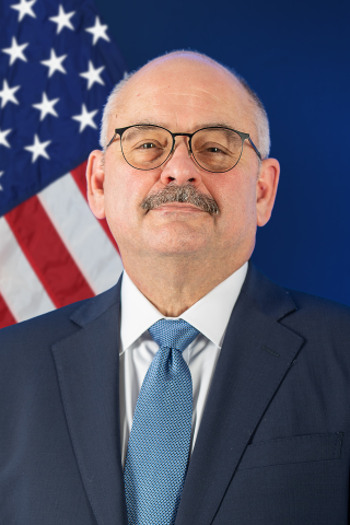 Man in suit and tie with US flag in background.