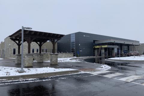 A dark grey panel and light stone building with a large four-post pergola beside the building entrance