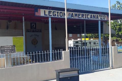 One story building, painted light cream with blue trims on roof, and a cream-colored fence at entrance. Building is identified with a sign on the roof that reads "Legion Americana"