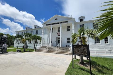 Image of the front facing white building which is the Miami Military Museum and Memorial. Above the face of the building reads 'Miami Military Museum and Memorial' in black. 