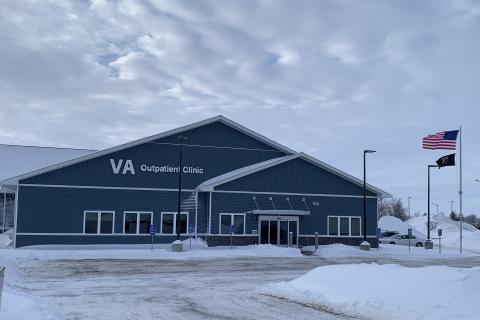 photo of a blueish gray building with a pitched roof and many glass windows on the front. There is a driveway in the front and snow on the ground.
