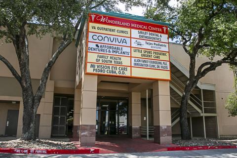 A tan colored building that is a mall entrance, surrounded by two trees