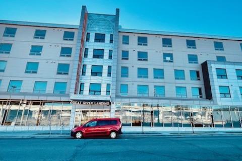 Large multilevel building with Great River Landing sign above main entrance of building. Ground level of building is mostly large glass windows