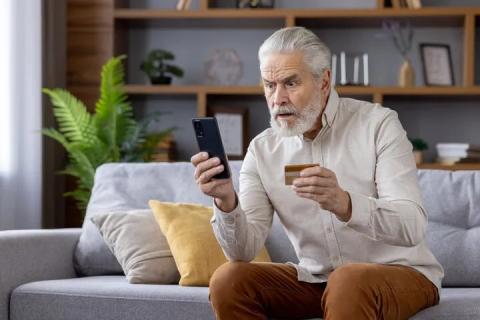 Man sitting on couch in front of a laptop holding a credit card