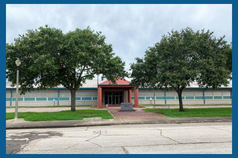 White and Blue building, Coral colored entrance. Large trees at the entry way.