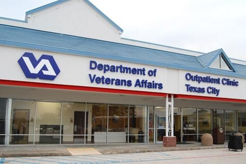 It is a white and blue building. It has blue text on it saying Department of Veteran Affairs Outpatient Clinic Texas City.