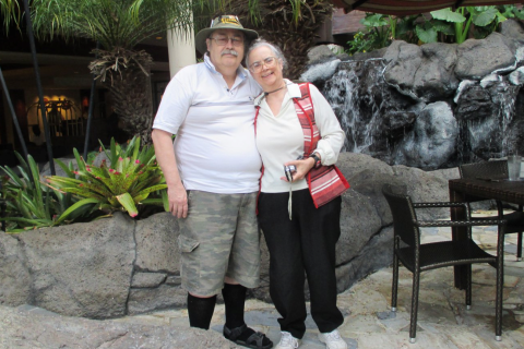 A couple smiling and posing together for a photograph in a scenic outdoor setting.