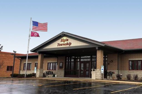 A brown building with two built-in pillars supporting a covered entrance and a nearby flagpole