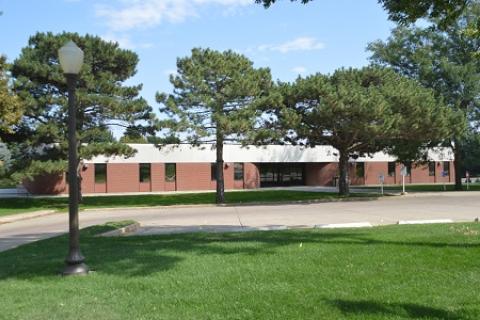 One story brick building with trees and parking lot in front. 