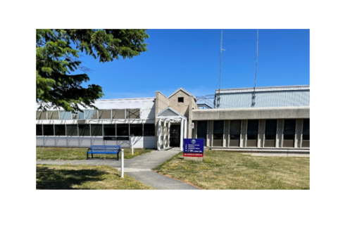 outdoors, clear blue sky,  building, grass, tree, bench in front of building next to sidewalk.