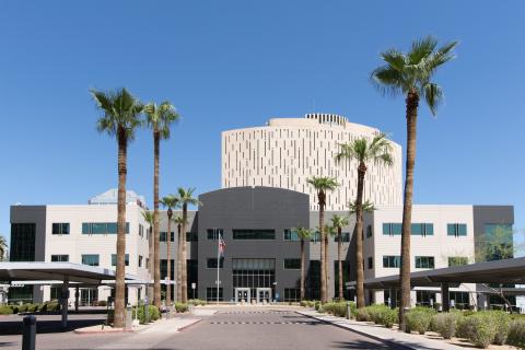 Outside of three story building, multicolor grey and beige. Front entrance to right side with glass doors. Visitor parking to left side of facility.   