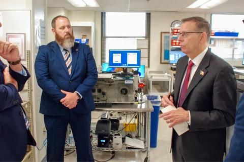Men in suits standing in a pharmacy workspace.