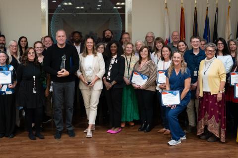 A large group of people posing in front of flags and a VA seal at the Spirit of George E. Wahlen Awards ceremony