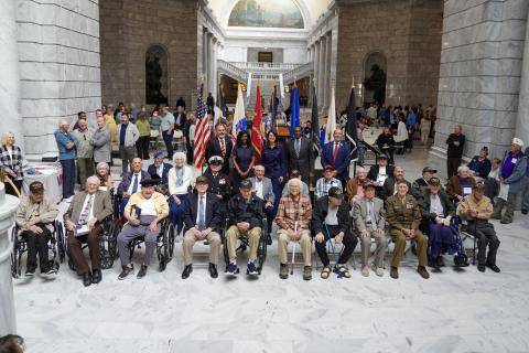 A groupf of 100-year-old Veterans sit in front of service flags after being honored by the state of Utah.