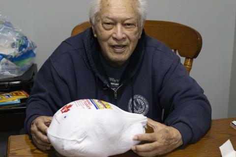 Veteran Papa Wong sits at a table holding a 10-pound frozen turkey gifted to him.