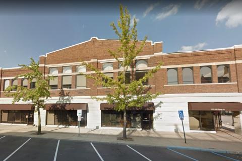 Exterior of brick building with trees and parking lot.