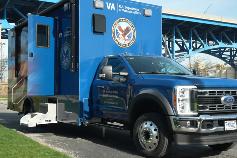 Blue ambulance truck with US Department of Veterans Affairs logo parked under a bridge.
