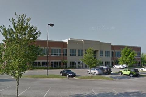 Office building with parking lot, several cars, and trees.