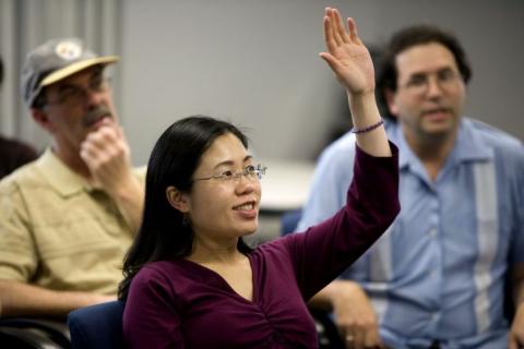 Woman with arm raised in a classroom full of people.