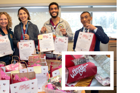 Four people holding signs stand behind a table of gift bags.