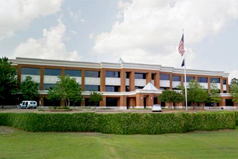 Modern office building with flag, surrounded by greenery and trees.