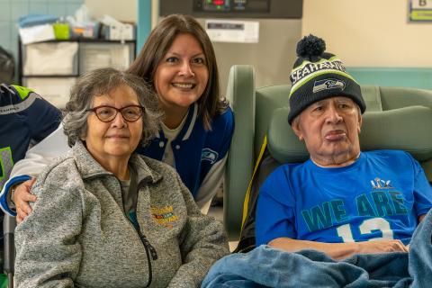 Veteran wearing Seahawks beanie and shirt accompanied by wife and daughter at VA Puget Sound Community Living Center's Super Bowl watch party.