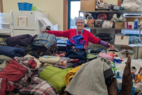 Woman with arms open in front of table full of winter coats and boots.