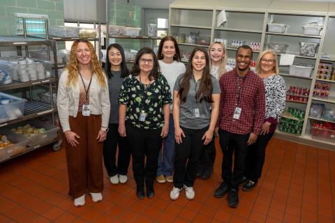 Nine staff members stand together in a kitchen, smiling for the camera.