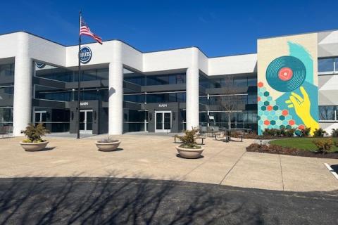 Modern white office building with colorful mural, flag, and clear blue sky.