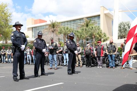 Three police officers standing at attention in front of a crowd during a ceremony.