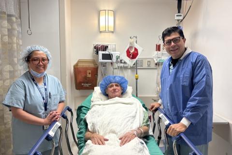 A patient in a hospital bed with two medical professionals prior to a procedure posing for a photo, all smiling.