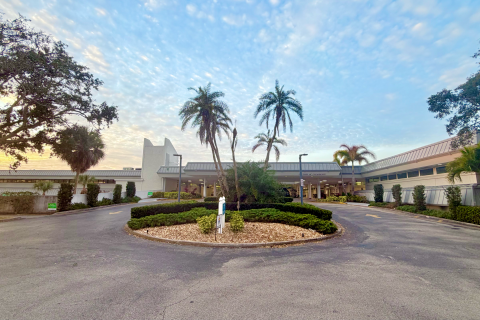 Empty circular driveway with palm trees and shrubs in front of a building.