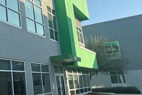 Gray office building with green accents, glass windows, and a tree in front.
