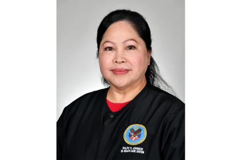 Woman in black uniform with red collar and badge smiling.