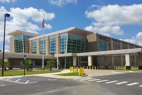Modern hospital building with large windows, flagpole, and pedestrian crossing.
