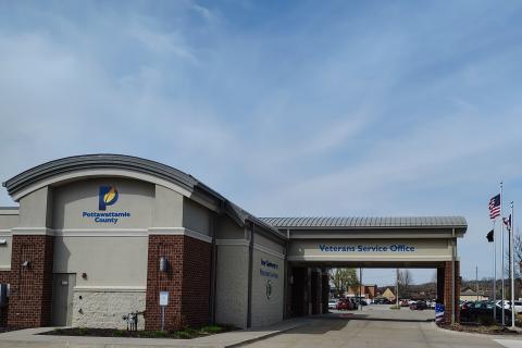 A modern building with a curved entrance, blue sky, and flagpoles.
