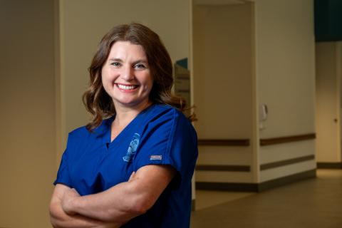 Woman in blue scrubs standing with arms crossed, smiling.