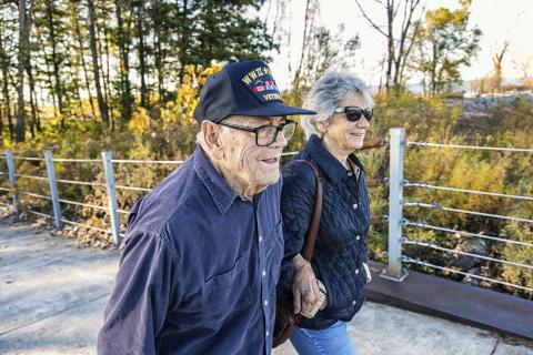 Elderly couple walking, man in navy cap, woman in sunglasses.
