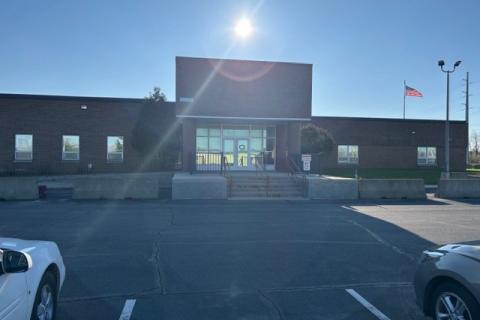 Two cars parked in front of a large building with flag and bright sun.