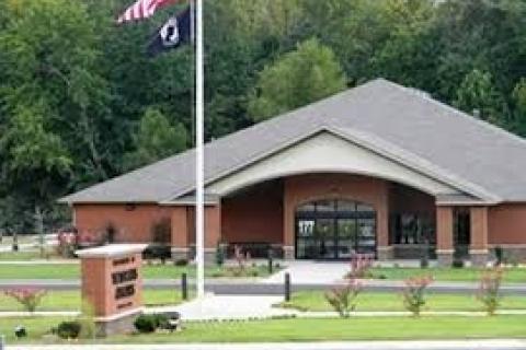 Building with gray roof and brown walls, two flags, and green lawn.
