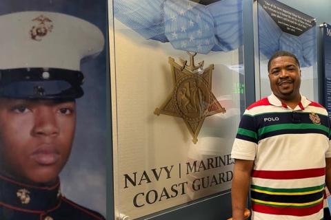 Man in striped shirt stands next to poster of Navy Coast Guard and military man.