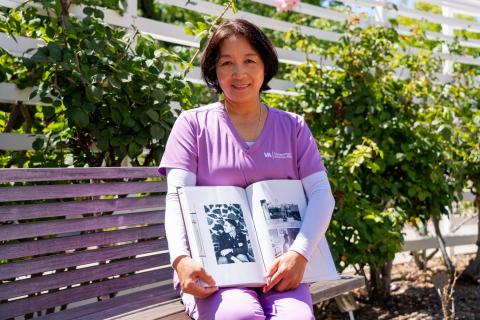 A woman in purple scrubs holds a photo album on a bench.