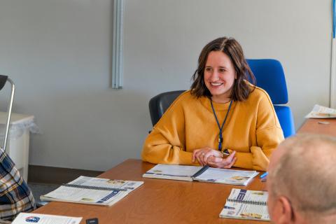 Woman in yellow shirt smiling at a table with pamphlets.